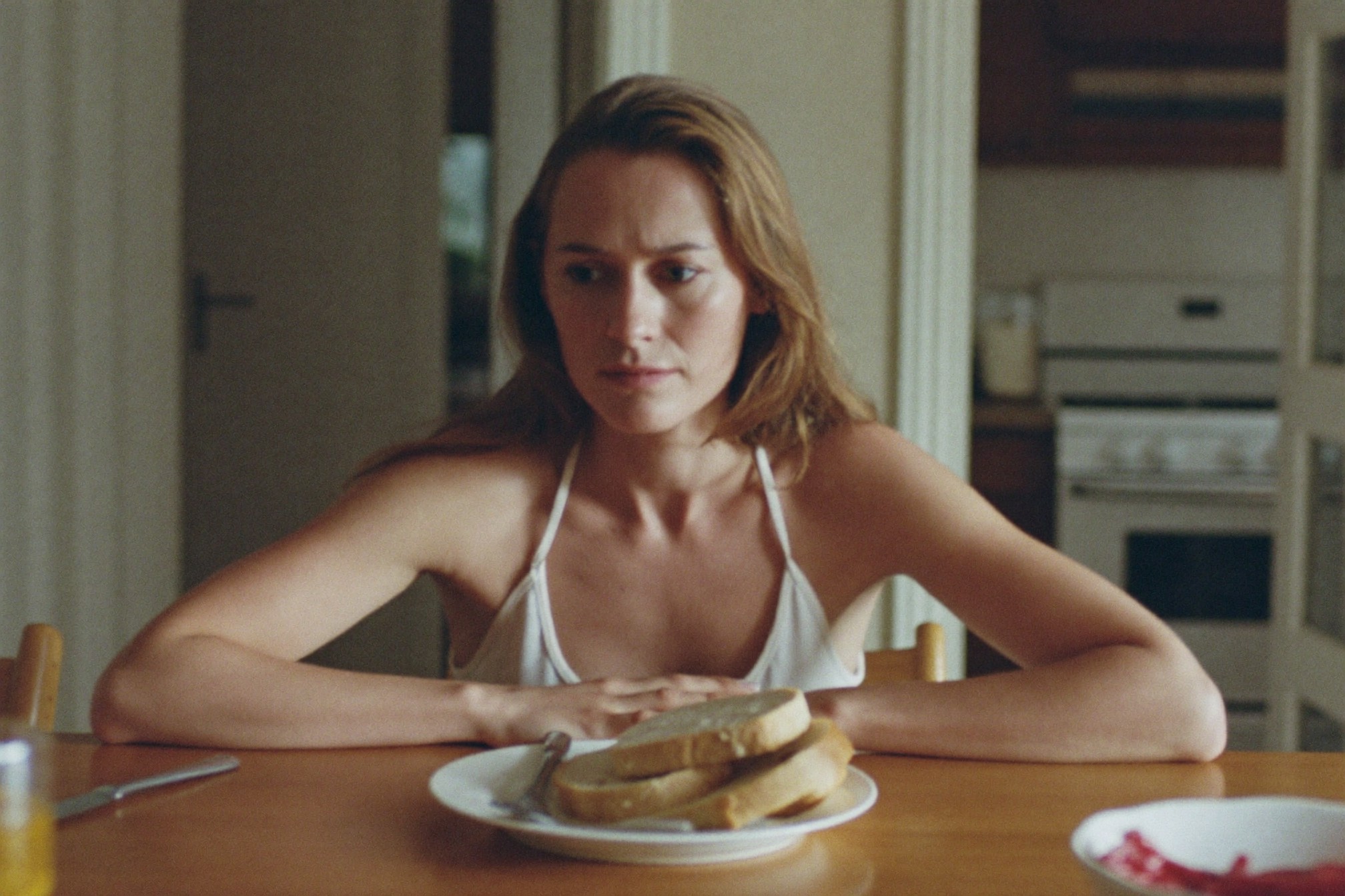 A woman at a table with a plate of bread, hand on her stomach