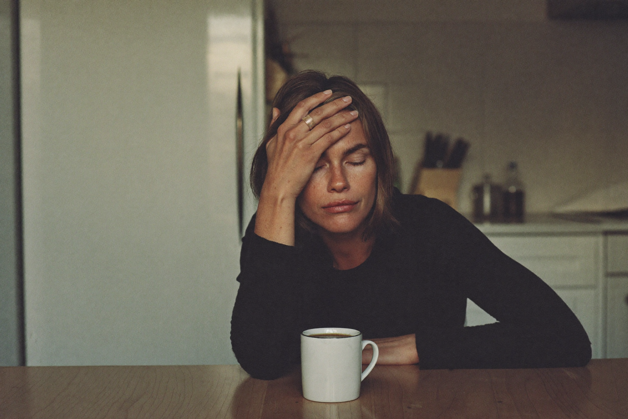 An exhausted woman resting her head in her hand at a kitchen table