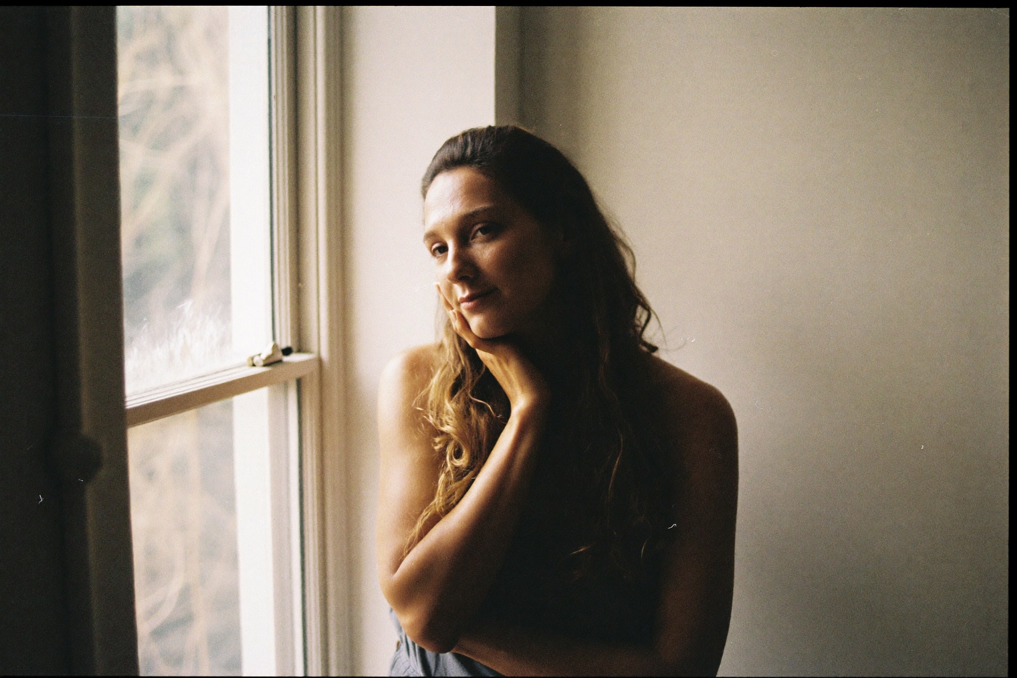 A woman by a window, hand resting on her cheek