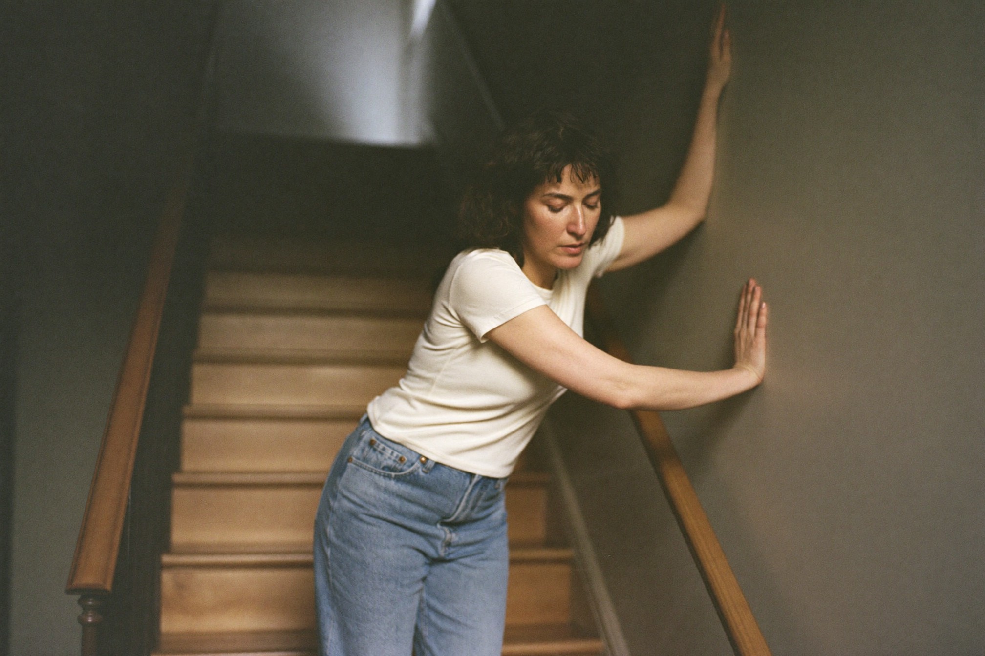 A woman pausing on a staircase, hand on the wall for balance
